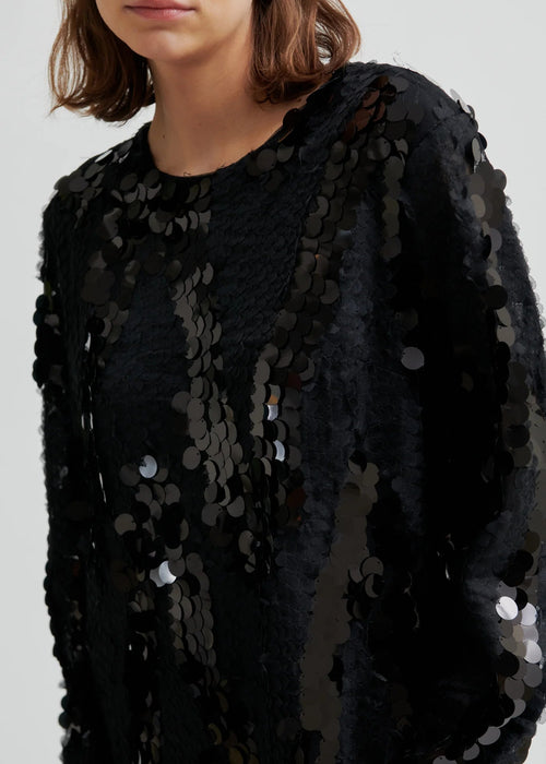 Woman wearing a black sequin dress with knee-high boots on a white background