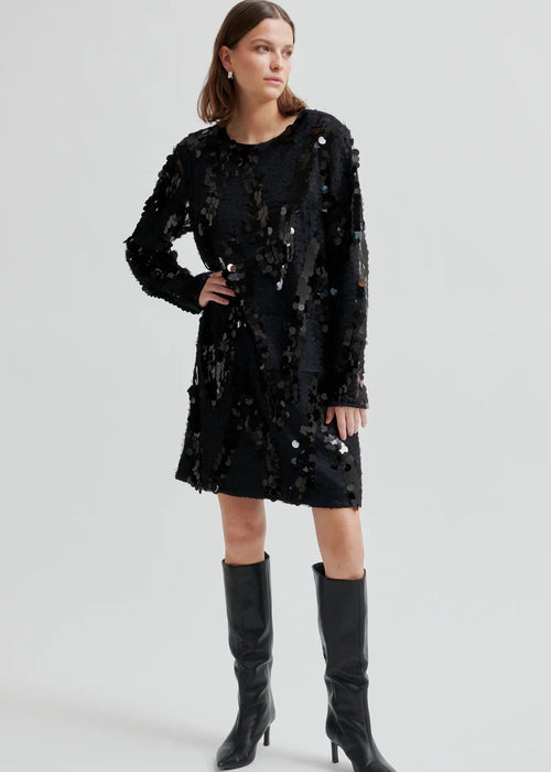 Woman wearing a black sequin dress with knee-high boots on a white background