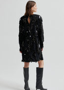 Woman wearing a black sequin dress with knee-high boots on a white background