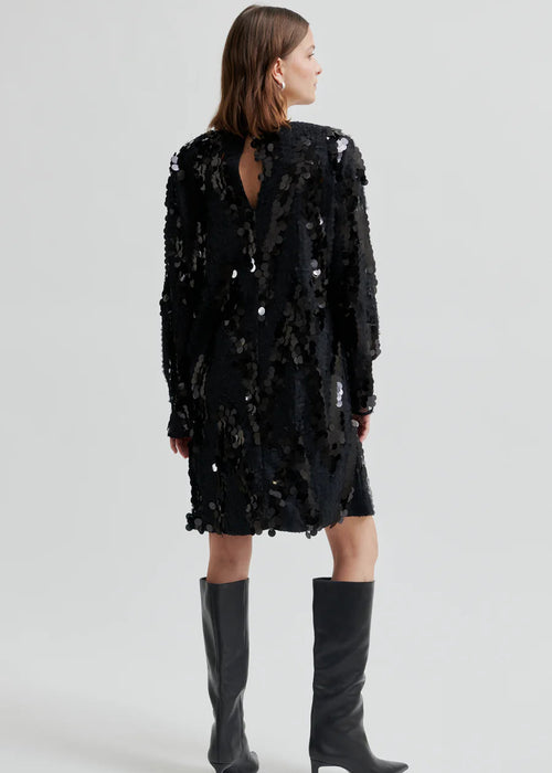 Woman wearing a black sequin dress with knee-high boots on a white background
