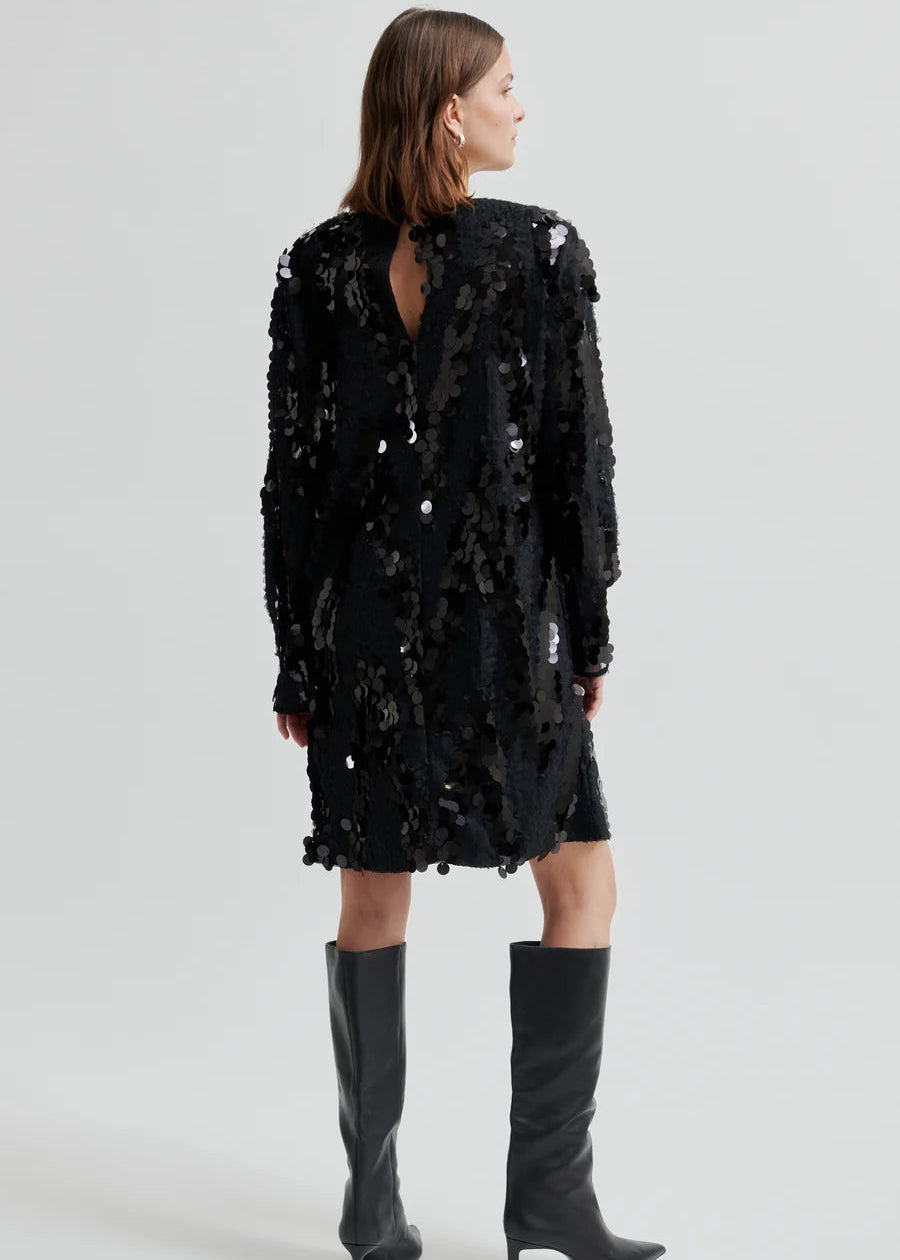 Woman wearing a black sequin dress with knee-high boots on a white background