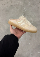 Beige sneaker held by a hand on a concrete floor