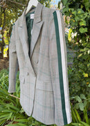 Gray checkered blazer with green accents hanging on a rack against a green foliage background