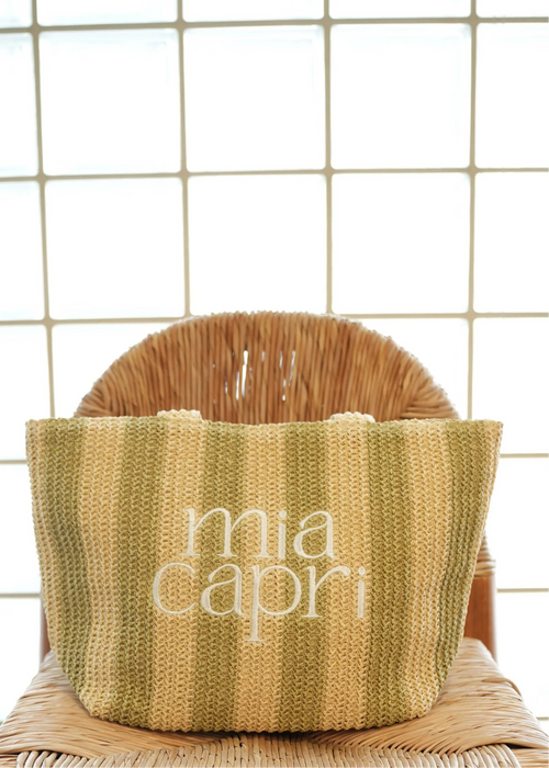 Striped bag with 'mia capri' branding on a wicker chair against a tiled wall.