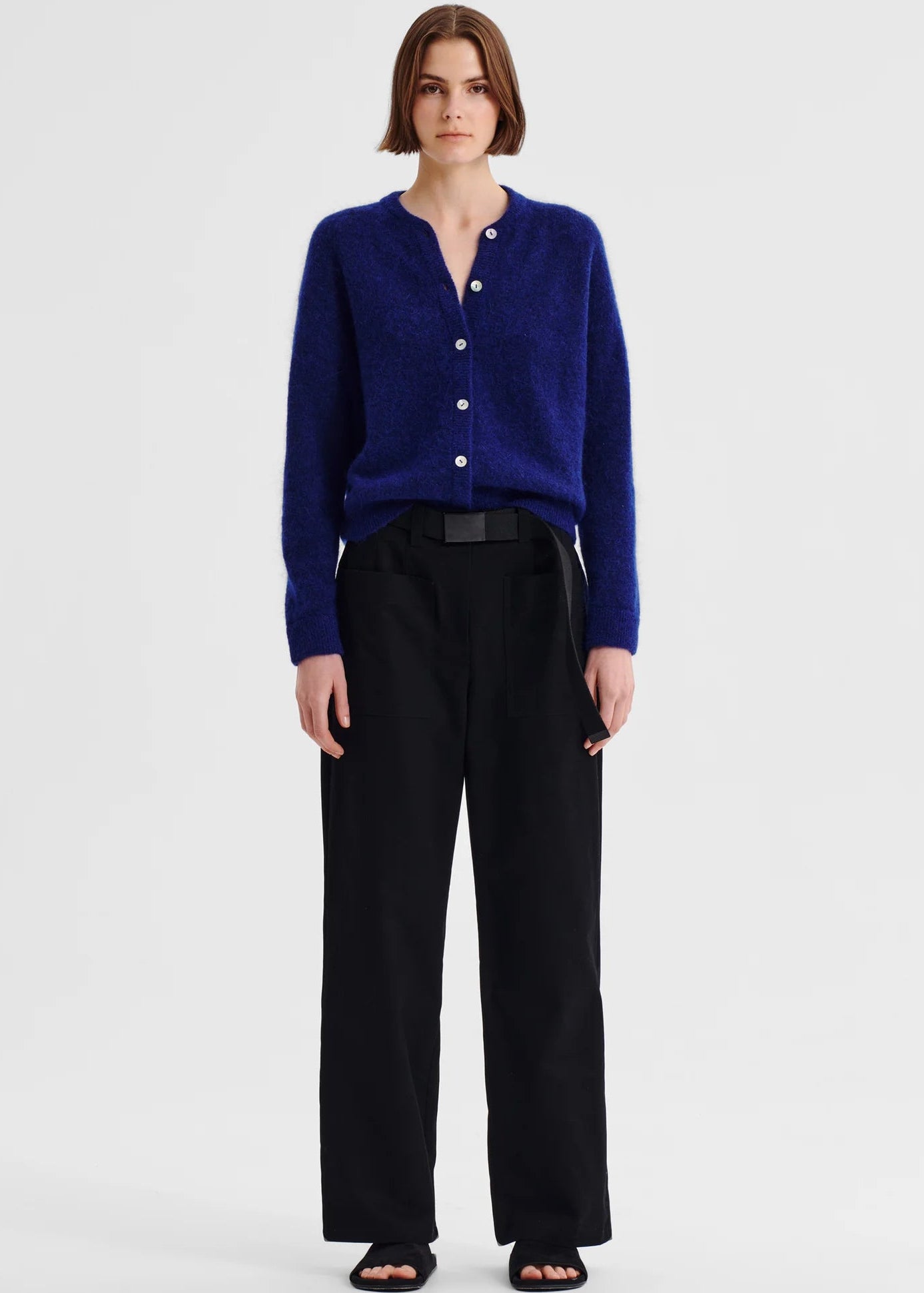 Woman wearing a blue cardigan and black pants on a white background