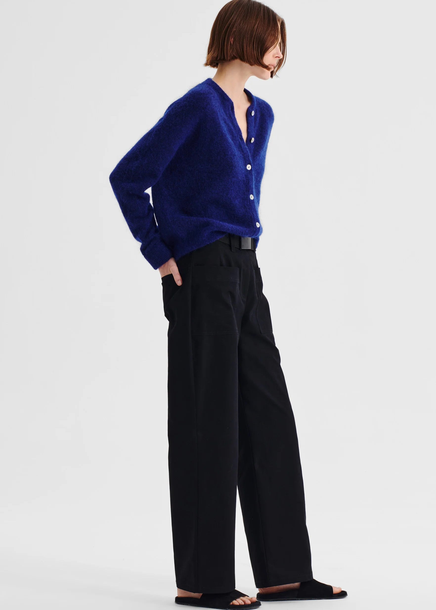 Woman wearing a blue cardigan and black pants on a white background