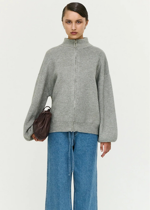 Person wearing a grey zip-up sweater and blue jeans on a white background