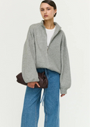 Person wearing a grey zip-up sweater and blue jeans on a white background