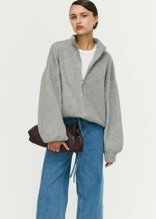 Person wearing a grey zip-up sweater and blue jeans on a white background