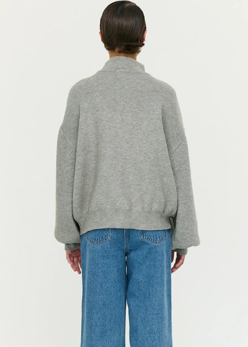 Person wearing a grey zip-up sweater and blue jeans on a white background