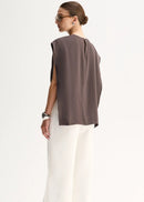 A woman shown from the back wearing a sleeveless taupe-brown top and white wide-leg trousers, photographed against a clean white studio background.