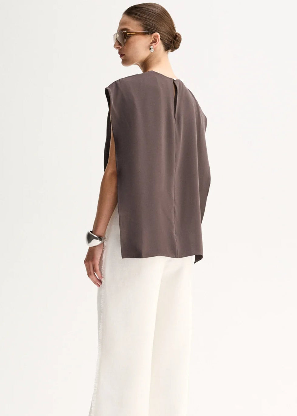 A woman shown from the back wearing a sleeveless taupe-brown top and white wide-leg trousers, photographed against a clean white studio background.