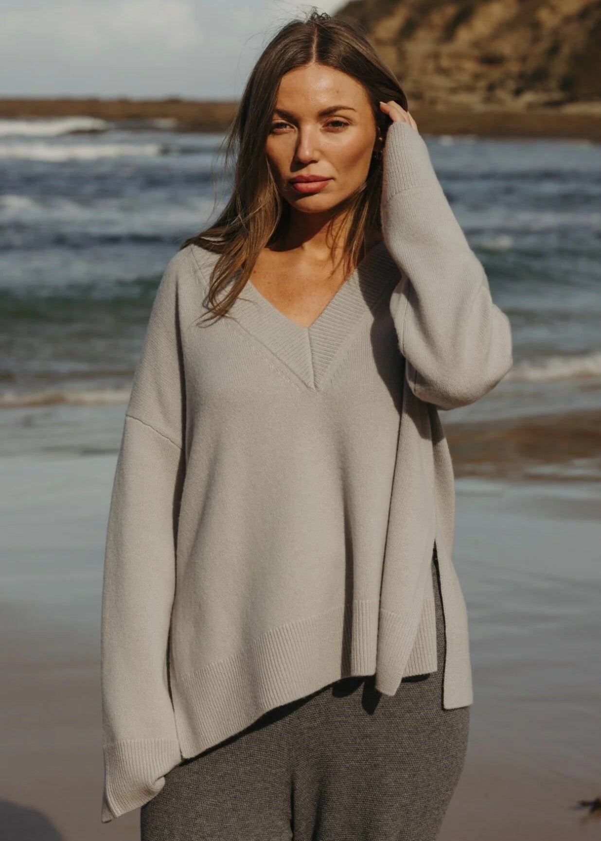 Woman standing on a beach wearing a grey sweater 