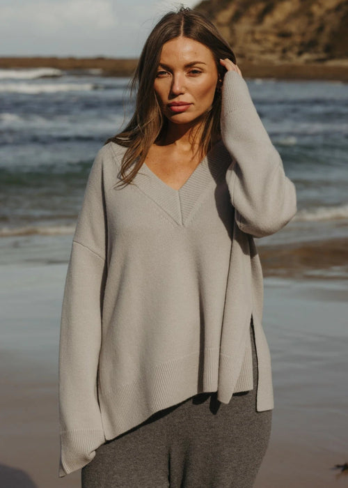 Woman standing on a beach wearing a grey sweater 
