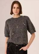 Woman wearing a dark grey top with decorative beading against a plain background