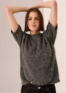Woman wearing a dark grey top with decorative beading against a plain background