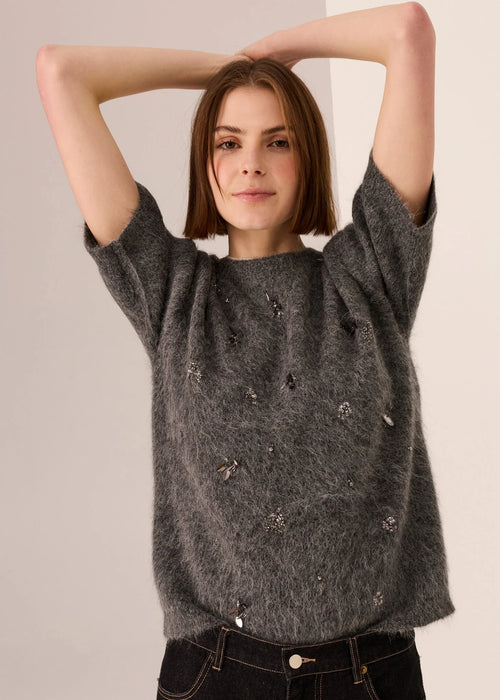 Woman wearing a dark grey top with decorative beading against a plain background
