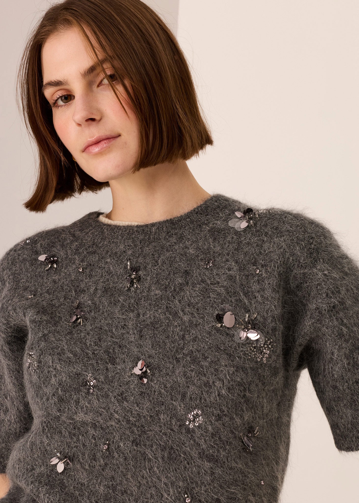 Woman wearing a dark grey top with decorative beading against a plain background