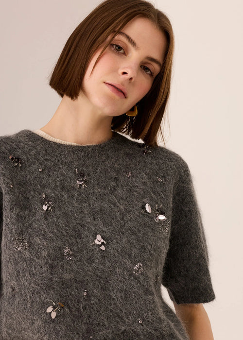 Woman wearing a dark grey top with decorative beading against a plain background