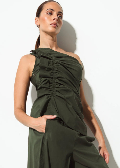 A woman modelling a dark olive green one-shoulder ruched dress with a draped bodice and wide-leg skirt against a plain white studio background.