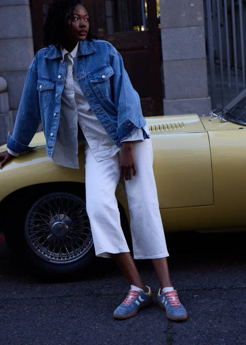 Person wearing a denim jacket and white pants standing next to a yellow car.