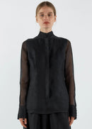 Person wearing a black blouse with sheer sleeves on a white background