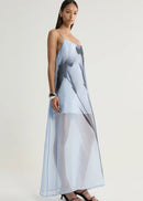 A woman modelling a sheer, light blue maxi dress with a large black abstract print, photographed against a neutral light grey studio background.