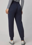 Woman wearing a striped long-sleeve top and navy jogger pants on a grey background