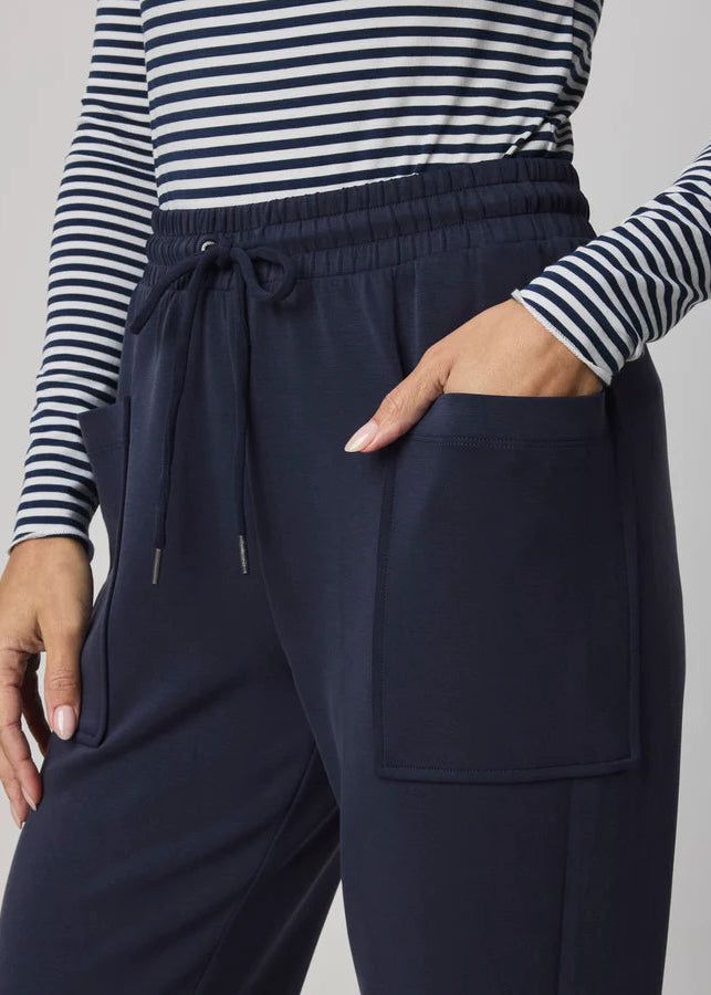 Woman wearing a striped long-sleeve top and navy jogger pants on a grey background