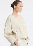 A model wearing a light beige cropped jacket with a front zipper and matching wide-leg trousers, photographed against a clean white studio background.