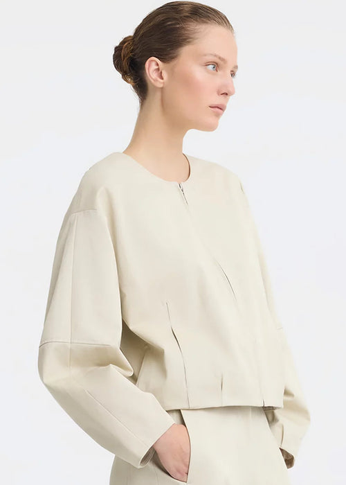 A model wearing a light beige cropped jacket with a front zipper and matching wide-leg trousers, photographed against a clean white studio background.