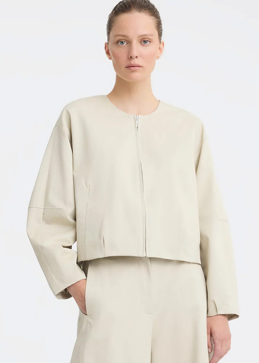 A model wearing a light beige cropped jacket with a front zipper and matching wide-leg trousers, photographed against a clean white studio background.
