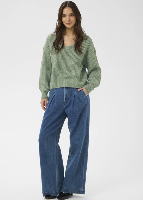 Woman wearing a green sweater and blue jeans on a white background