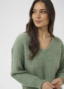 Woman wearing a green sweater and blue jeans on a white background