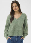 Woman wearing a green sweater and blue jeans on a white background