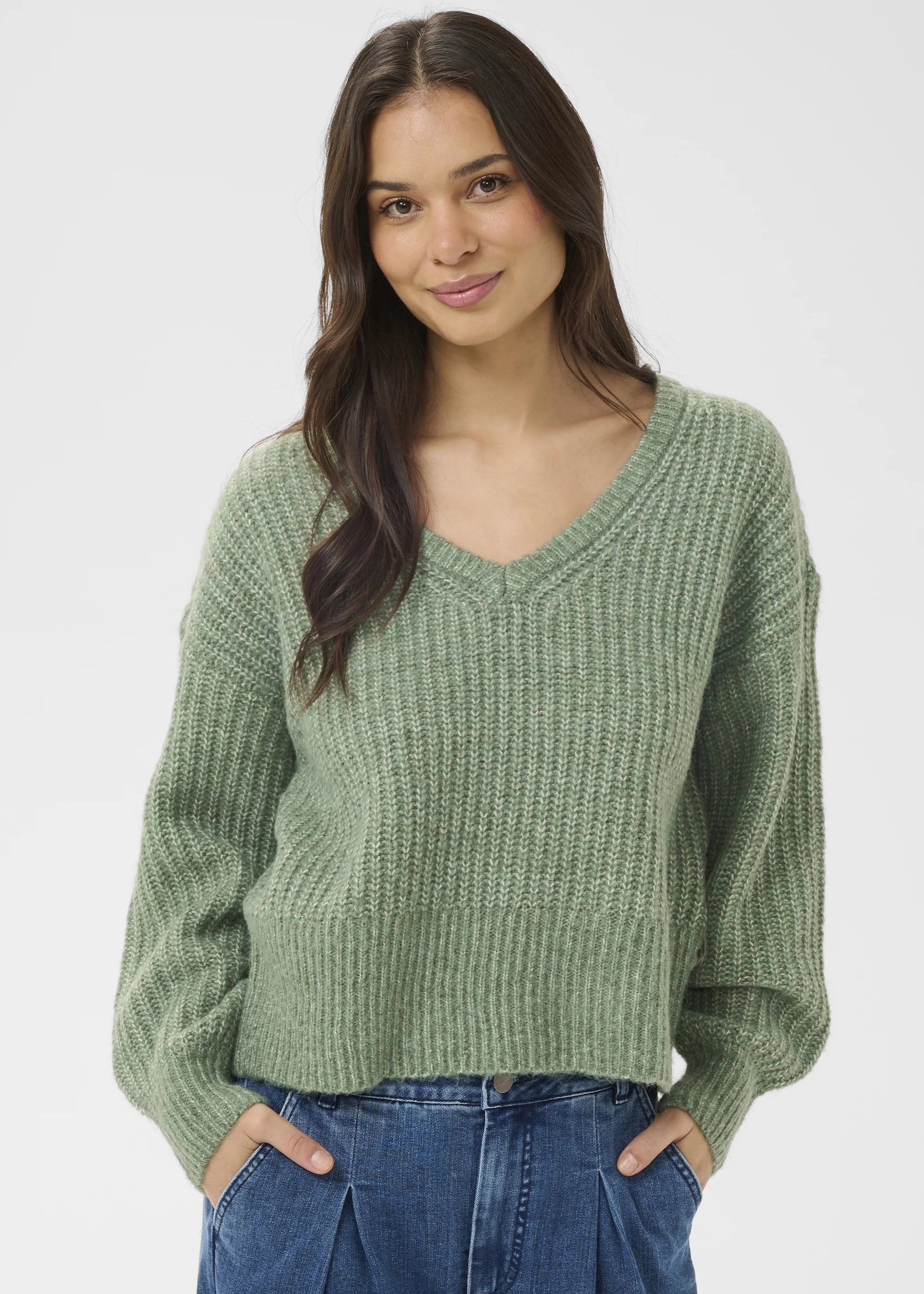 Woman wearing a green sweater and blue jeans on a white background