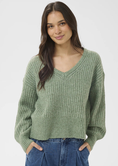 Woman wearing a green sweater and blue jeans on a white background
