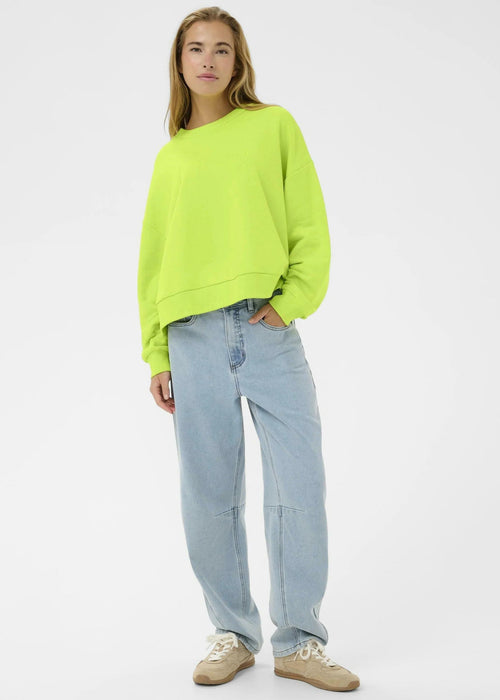 Woman wearing a bright green sweatshirt and light blue jeans on a white background