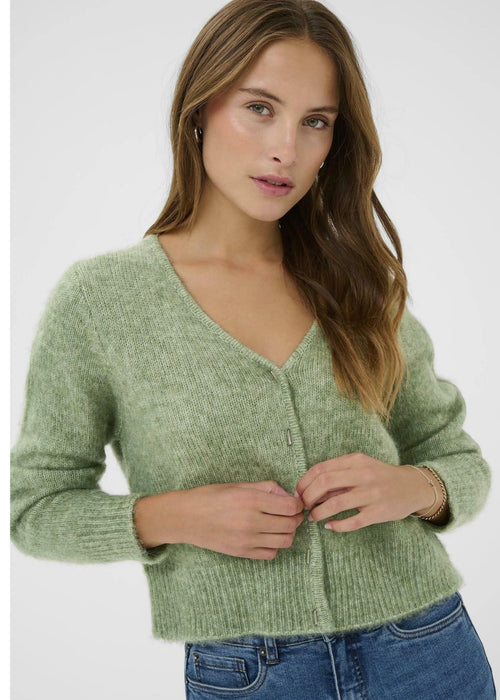 Woman wearing a green cardigan and blue jeans on a white background