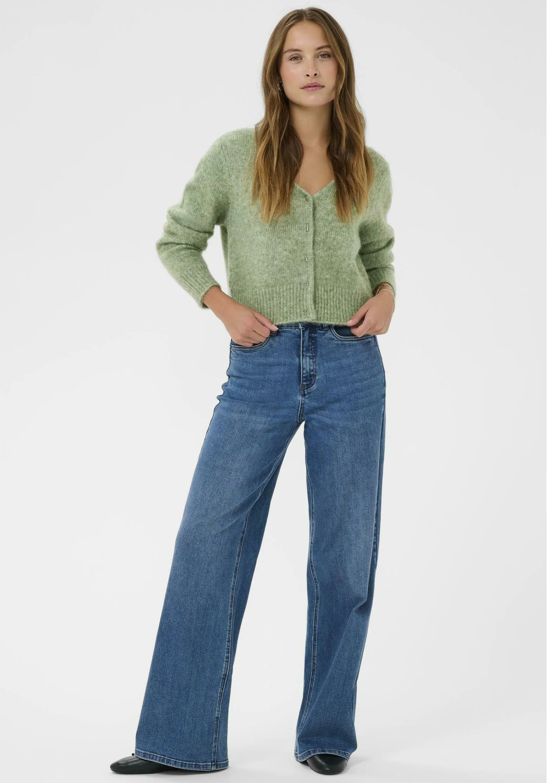 Woman wearing a green cardigan and blue jeans on a white background