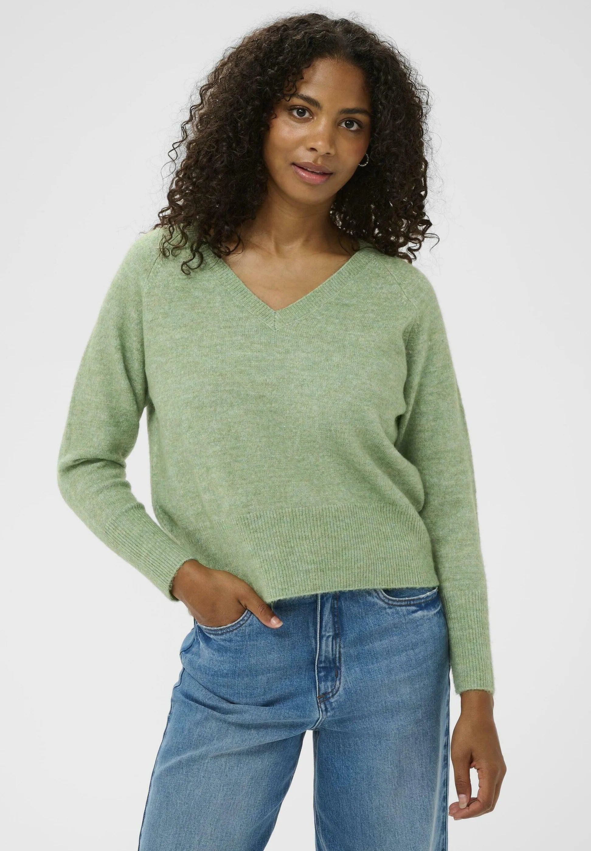 Woman wearing a green sweater and blue jeans on a white background