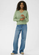 Woman wearing a green sweater and blue jeans on a white background