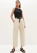 Woman wearing a black sleeveless top and beige high-waisted pants on a white background