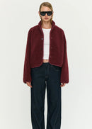 Woman wearing a burgundy jacket, white top, and dark jeans on a white background