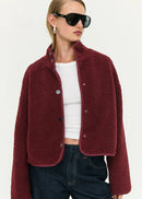 Woman wearing a burgundy jacket, white top, and dark jeans on a white background