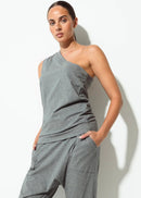 A woman modelling a grey two-piece loungewear set consisting of a one-shoulder tank top and matching jogger pants, paired with black and white flip-flop sandals, set against a plain white studio background.
