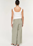 A model wearing a white sleeveless top, wide-leg striped trousers in beige and green, sunglasses, and holding a dark woven handbag against a plain white studio background.