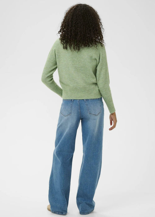 Woman wearing a green sweater and blue jeans on a white background