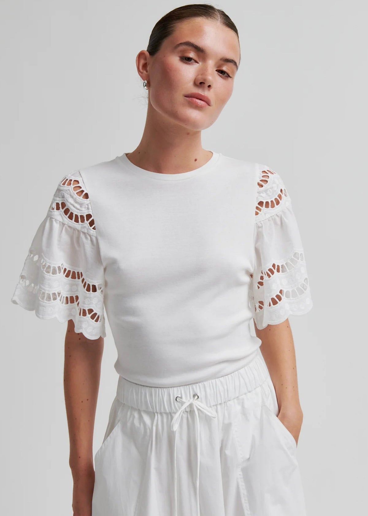 Woman wearing a white outfit with decorative sleeves on a plain background