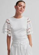 Woman wearing a white outfit with decorative sleeves on a plain background